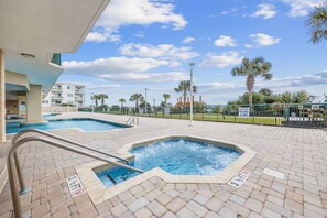 Un área de piscina con jacuzzi, piscina y zona vallada con palmeras.