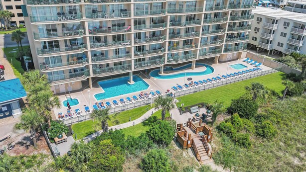 Un hotel de varios pisos con piscina en la azotea, que incluye sillas de descanso y una pequeña terraza.