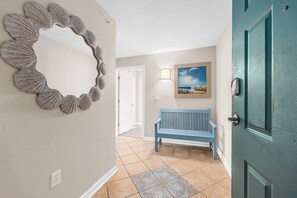 A hallway with a decorative mirror, a bench, and a door.