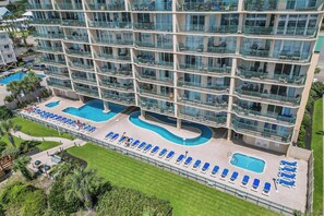 A multi-story hotel with balconies, a swimming pool, and sun loungers. - Oceanfront Luxury Top Location Lazy River Pool Grills (North Myrtle Beach)