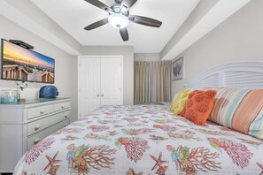 A bedroom with a bed, a ceiling fan, a dresser, a TV, and a door.