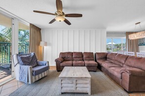 A living room with a brown leather sectional sofa, a wooden coffee table, and a ceiling fan. - Oceanfront Luxury Top Location Lazy River Pool Grills (North Myrtle Beach)