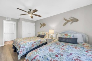 A bedroom with two beds, a ceiling fan, a nightstand with a lamp, and decorative wall art. - Oceanfront Luxury Top Location Lazy River Pool Grills (North Myrtle Beach)