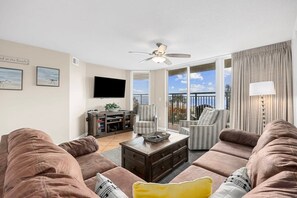 Ein Wohnzimmer mit Deckenventilator, Flachbildfernseher und Balkon mit Vorhängen.