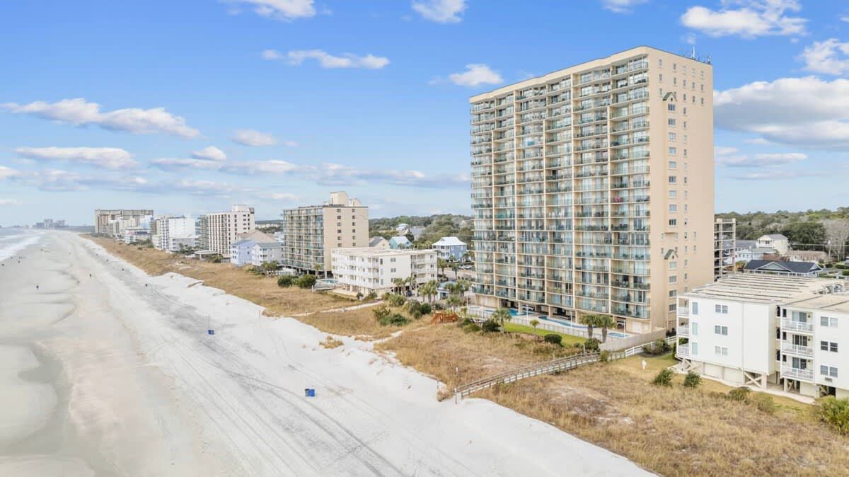 A beachfront hotel with multiple high-rise buildings, a sandy beach, and a clear sky.