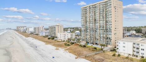A beachfront hotel with multiple high-rise buildings, a sandy beach, and a clear sky.