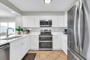 A modern kitchen with white cabinets, stainless steel appliances, and a large refrigerator. - Oceanfront Luxury Top Location Lazy River Pool Grills (North Myrtle Beach)