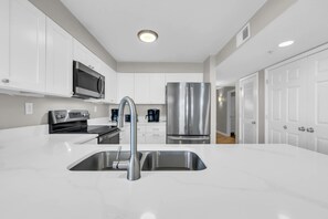 A modern kitchen with white cabinetry, stainless steel appliances, and a central sink.