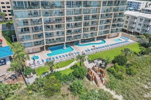 Un hotel de varios pisos con piscina en la azotea, que incluye sillas de descanso y una pequeña terraza.