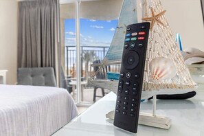 Un control remoto sobre una mesa de vidrio con un modelo de barco decorativo y conchas marinas.