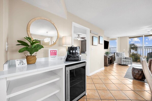 A hotel room with a kitchenette, a large mirror, a plant, a 'No Smoking' sign, a bag, and a view of the outdoors.