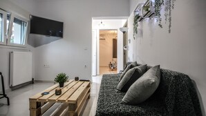 A modern living room with a sofa, a wooden table, and a TV mounted on the wall. - Terra di Meteora Suites 3 (Kalabaka)