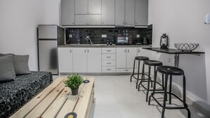 A compact kitchen with grey cabinets, a microwave, and a toaster. There is a small table with stools and a potted plant. - Terra di Meteora Suites 3 (Kalabaka)
