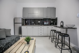 A compact kitchen with grey cabinets, a microwave, and a toaster. There is a small table with stools and a potted plant.
