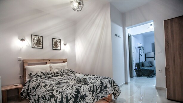 A modern bedroom with a wooden bed, a nightstand, and a wall-mounted light fixture. - Terra di Meteora Suites 3 (Kalabaka)