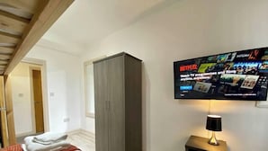 Ein Hotelzimmer mit Bett, Schrank, Wandfernseher und Nachttisch mit Lampe.