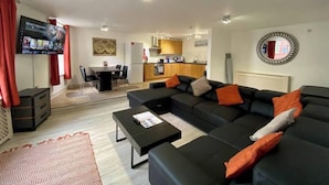 Ein modernes Wohnzimmer mit einer schwarzen Couch, einem Couchtisch und einem an der Wand montierten Fernseher.