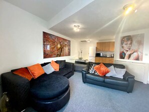 Relax in this stylish living space with a large sofa, kitchen area, and artwork on the walls.