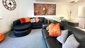 Un salon moderne avec un canapé d’angle, une horloge murale ronde et un grand tableau abstrait.