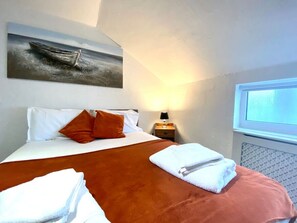 Relax in this serene hotel room with a comfortable bed, a beautiful painting of a boat, and a window offering a view of the sky.