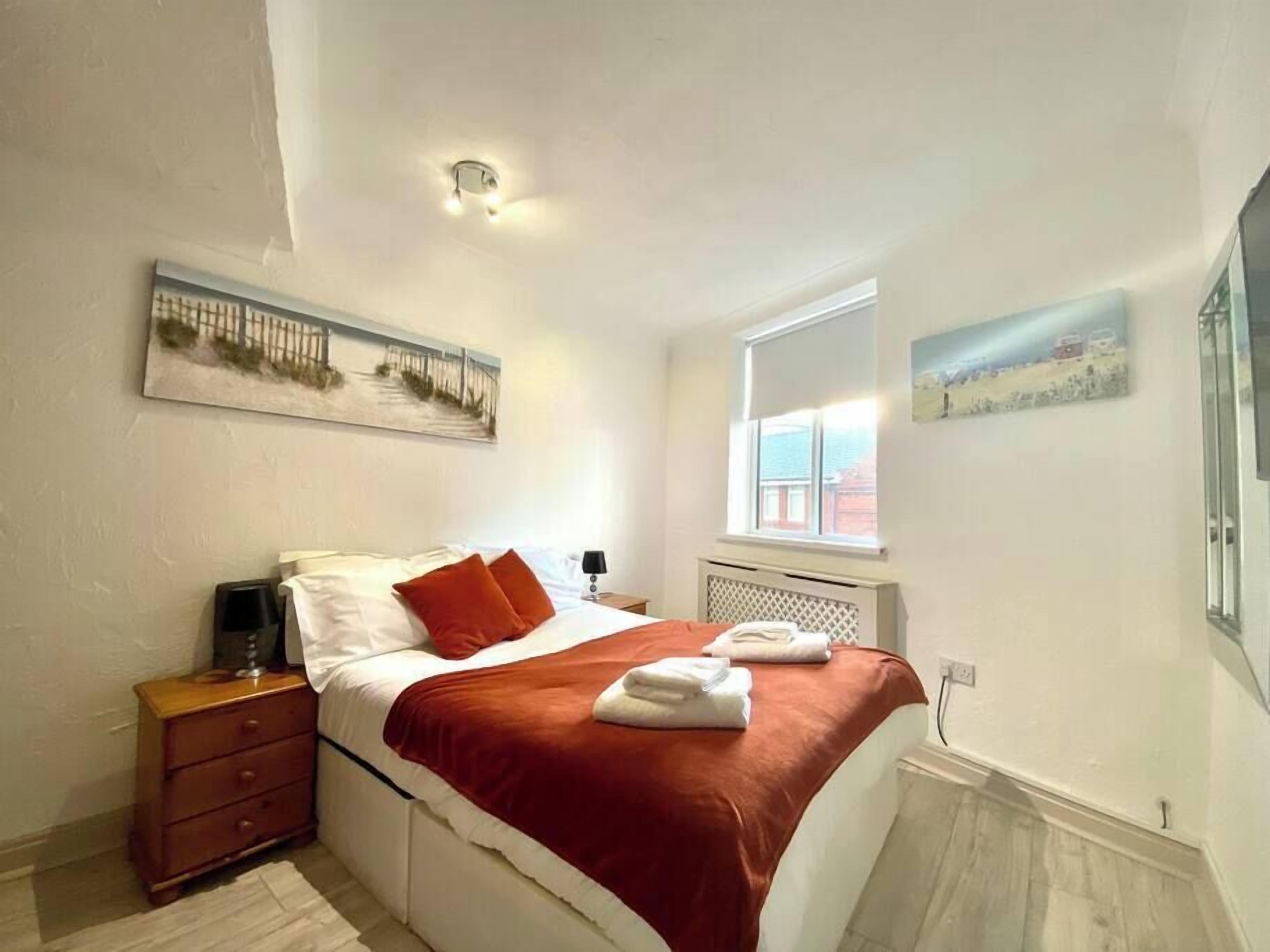 A bedroom with a bed, a nightstand, a window, and artwork on the walls.
