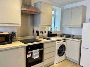 A compact kitchen with a microwave, oven, washing machine, and a sink.