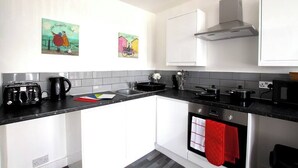 A modern kitchen with white cabinets, a black countertop, a stainless steel range hood, and two wall-mounted paintings.