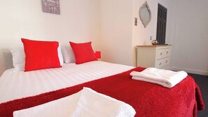 A hotel room with a bed, red and white bedding, a red throw blanket, and a white towel.