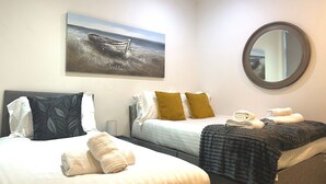 A hotel room with two beds, a painting of a boat on water, a round mirror, and neatly folded towels.