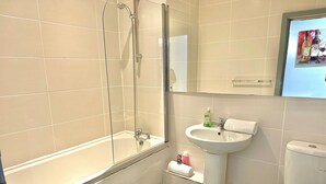 A bathroom with a bathtub, a sink, a toilet, and a trash can.