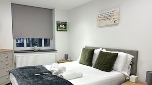Ein modernes Schlafzimmer mit Bett, Nachttischen, Heizkörper, Fenster und Wandbild.