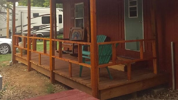 Una cabaña de madera con un porche, una puerta verde y un banco.