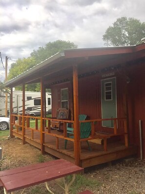 Una cabaña de madera con un porche, una puerta verde y un banco.