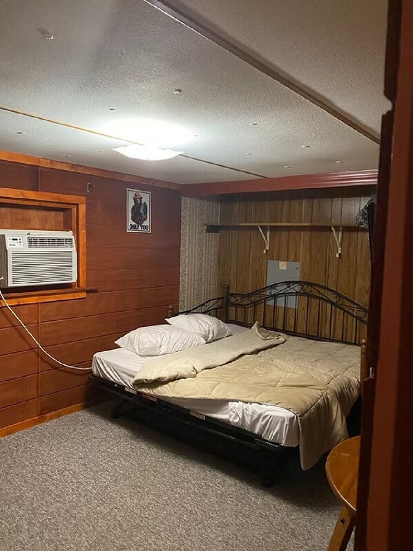 A small, single-bed room with wooden paneling, a ceiling fan, and an air conditioning unit.