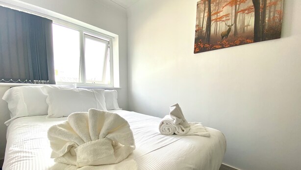 A hotel room with a neatly made bed, a window with curtains, and a painting on the wall.