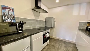 A kitchen with white cabinets, a black countertop, a stainless steel range hood, and a poster on the wall.