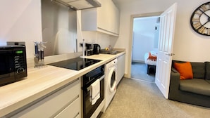 A compact kitchen with a microwave, kettle, and washing machine. - Winter Gardens Service Apartment 2 (Blackpool)