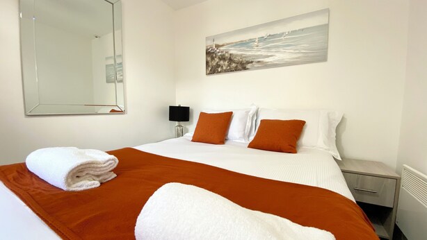 A hotel room with a bed, a painting, a nightstand, and a radiator. - Winter Gardens Service Apartment 2 (Blackpool)