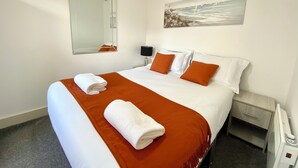 A hotel room with a large bed, a nightstand, a lamp, a painting, and a mirror. - Winter Gardens Service Apartment 2 (Blackpool)