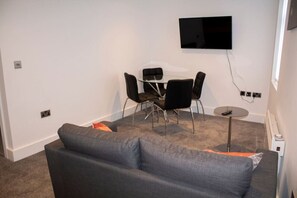 Cozy living space with a sofa, coffee table, and dining area featuring a flat-screen TV.