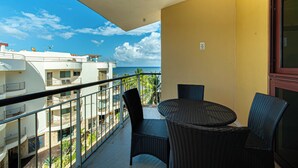A balcony with wicker furniture, a view of the sea, and a building with balconies. - Nice Caribbean style apartment in beachfront condominium (Playa del Carmen)
