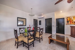 A dining area with a glass table, wooden chairs, and a ceiling fan.