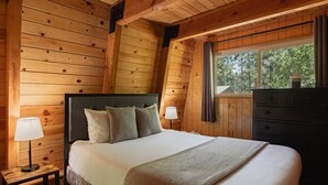 A wooden cabin bedroom with a bed, bedside lamps, and a dresser.