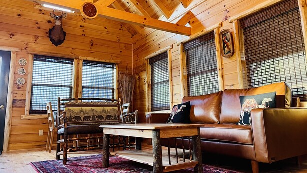 A cozy log cabin interior with a wooden ceiling, a leather sofa, a dining table, and a decorative deer head. - Cabin Sweet Cabin    (laurelville)