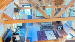 A wooden cabin interior with a balcony, a dining area, and a living room with a sofa and a coffee table. - Cabin Sweet Cabin    (laurelville)