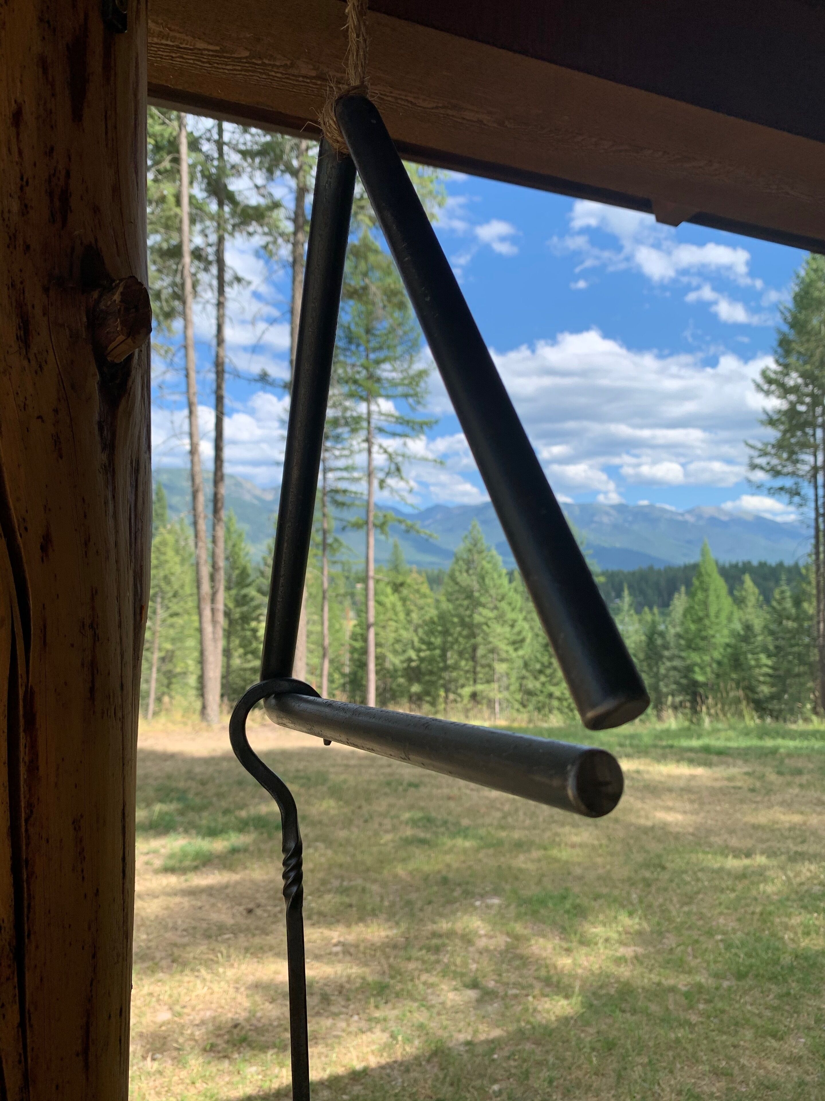 Una construcción rústica de madera con un gancho de metal y vistas a un bosque y montañas a través de una ventana.