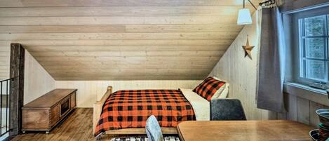 Ein gemütliches Schlafzimmer im Dachgeschoss mit Holzbalkendecke, einem Bett mit kariertem Überwurf, einem kleinen Nachttisch aus Holz und einem Fenster mit Vorhängen.