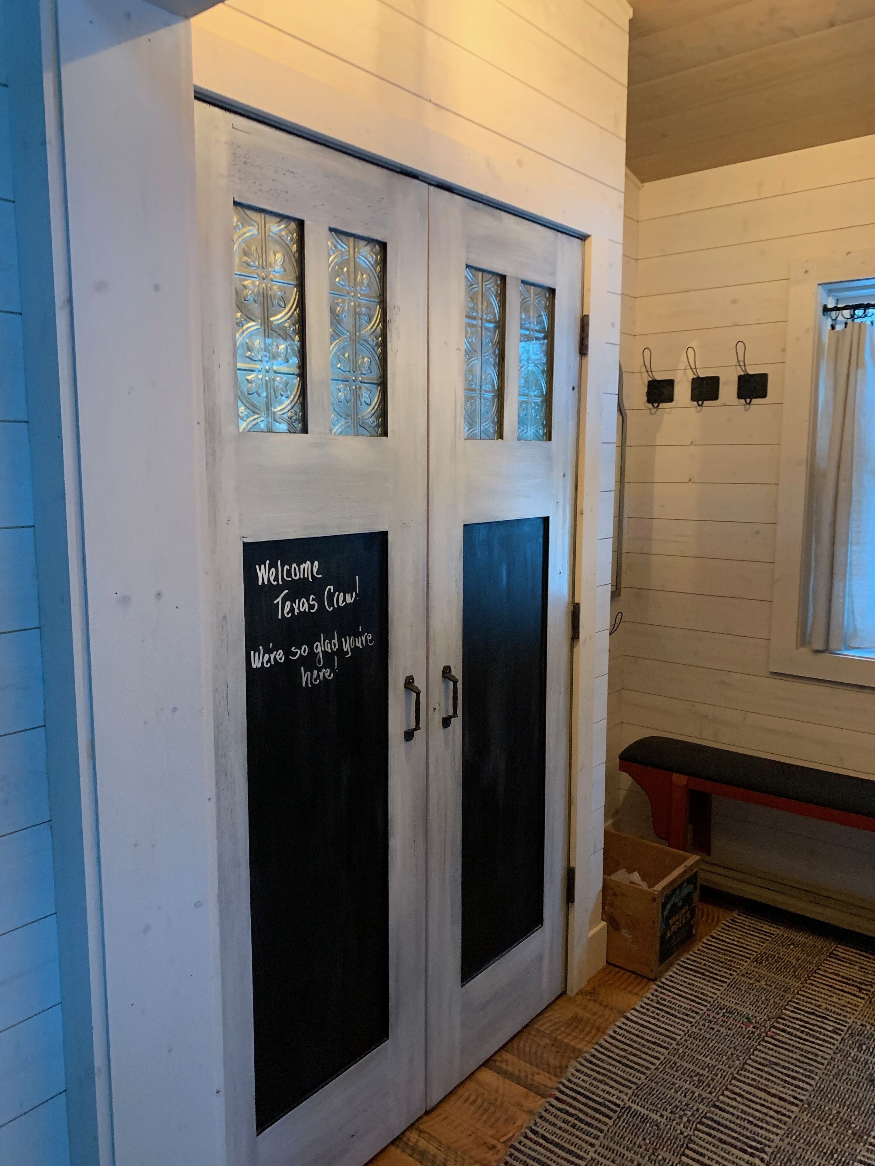 A room with a white door featuring a welcome message, a bench, and a window with curtains.