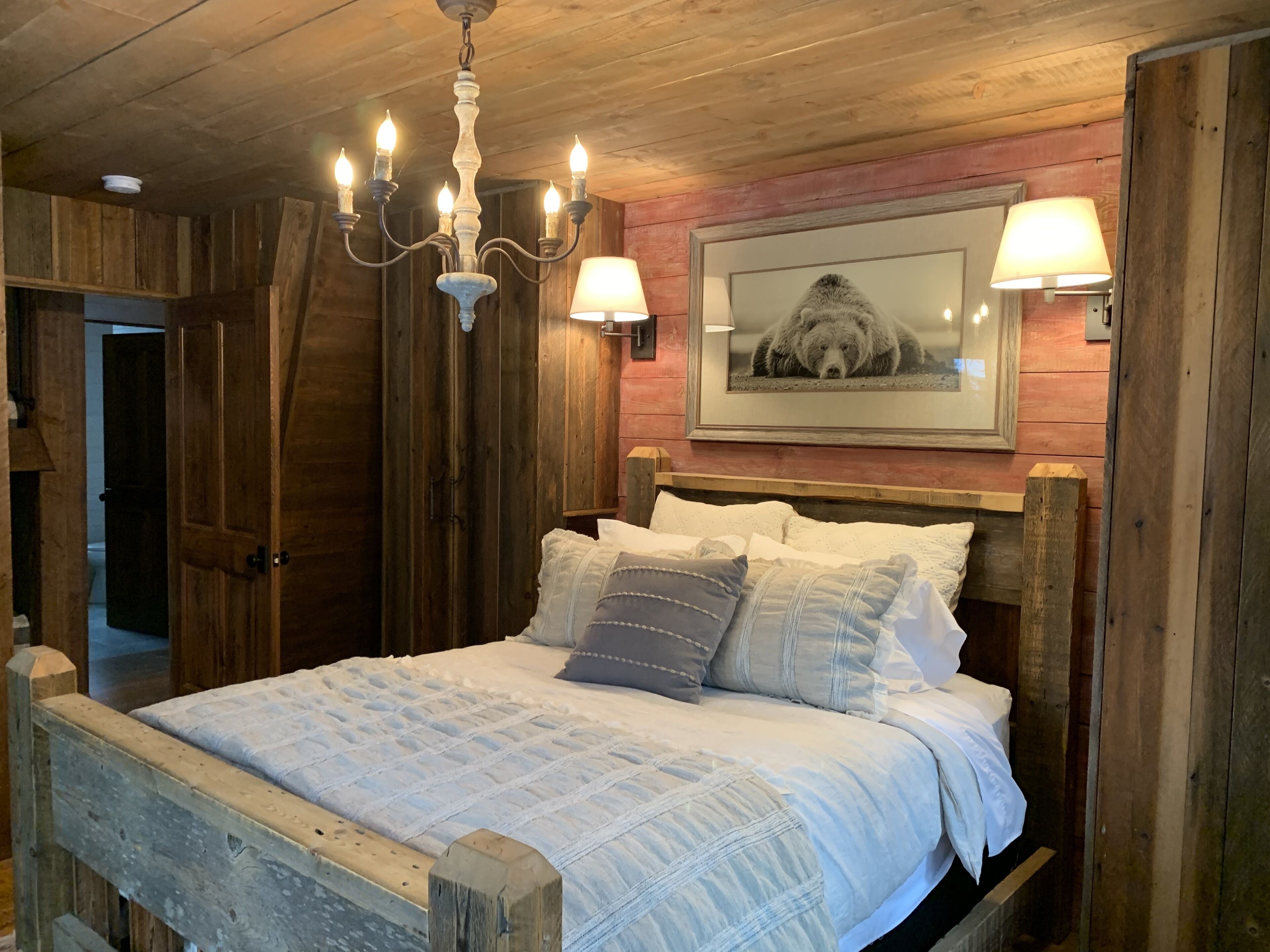 Een rustieke slaapkamer met een houten bed, een kroonluchter en een beren afbeelding aan de muur.