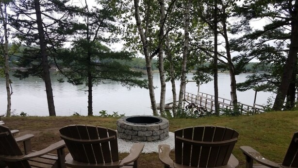 Een zitgedeelte aan het meer met Adirondack-stoelen en een vuurkorf van steen.